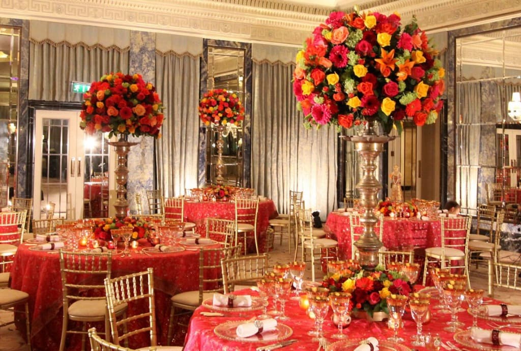 Grand royal wedding banquet hall with vibrant red floral arrangements and golden tableware